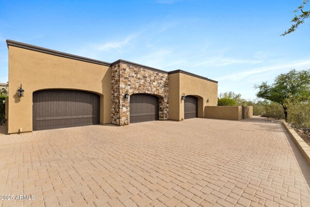 view of front of property featuring decorative driveway, a garage, stucco siding, and stone siding