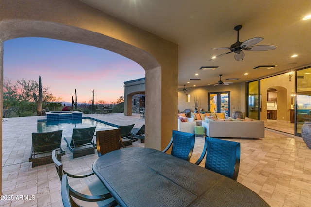 patio terrace at dusk with ceiling fan, outdoor lounge area, outdoor dining area, visible vents, and a pool with connected hot tub