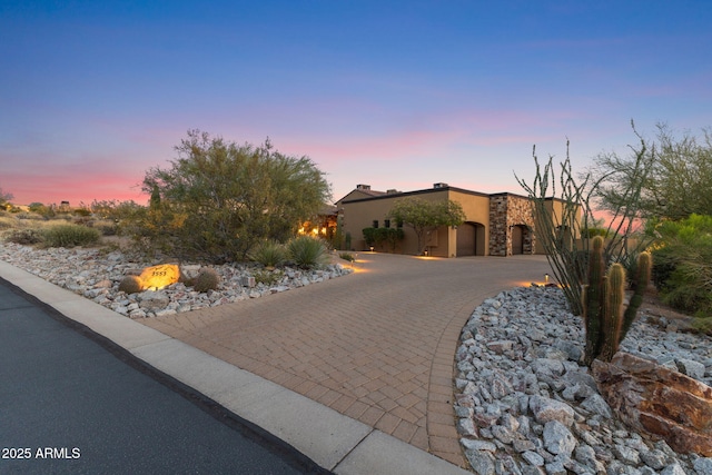 view of front of property featuring curved driveway, stucco siding, and stone siding