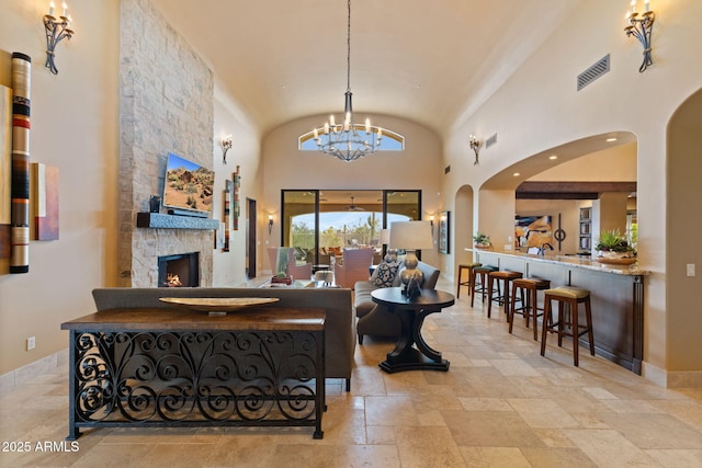 entrance foyer with a notable chandelier, high vaulted ceiling, a stone fireplace, visible vents, and stone tile flooring
