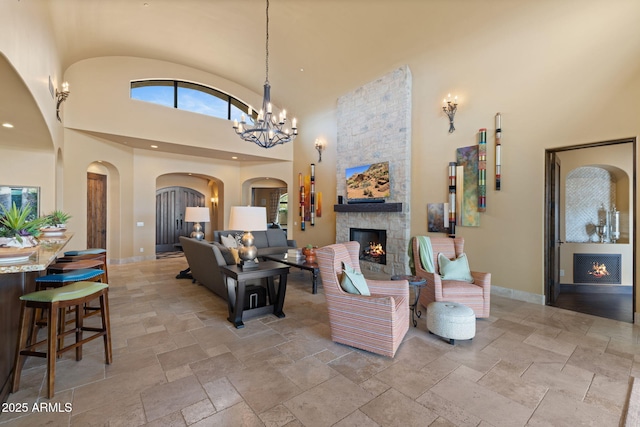 living area with baseboards, a fireplace, stone tile floors, and a towering ceiling