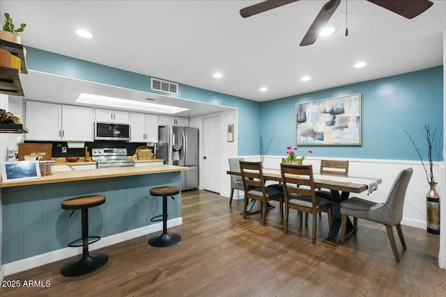 kitchen featuring a kitchen breakfast bar, dark wood finished floors, appliances with stainless steel finishes, a peninsula, and light countertops