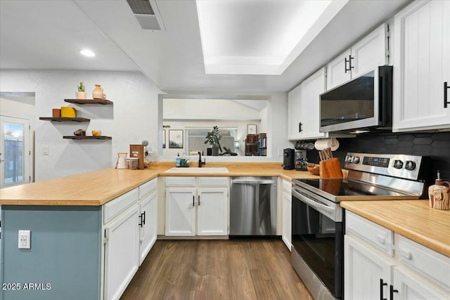 kitchen featuring visible vents, a sink, open shelves, appliances with stainless steel finishes, and a peninsula