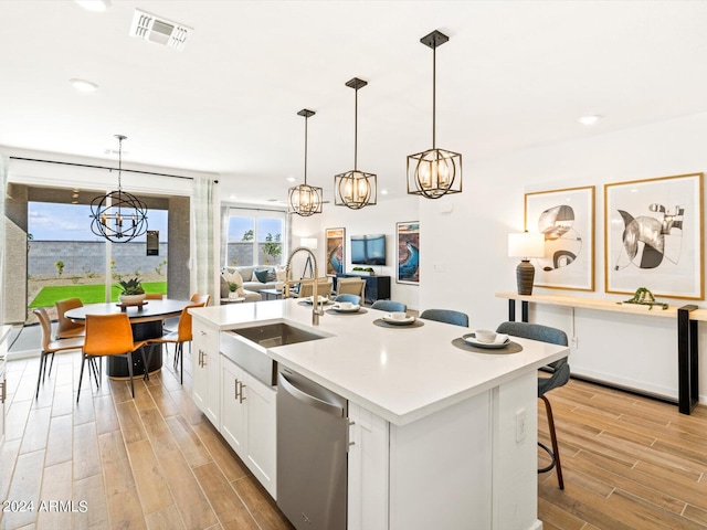 kitchen with white cabinets, stainless steel dishwasher, decorative light fixtures, and light hardwood / wood-style floors