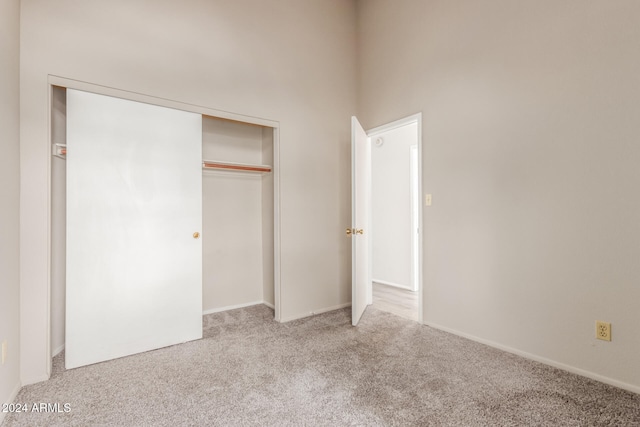 unfurnished bedroom featuring a towering ceiling, light carpet, and a closet