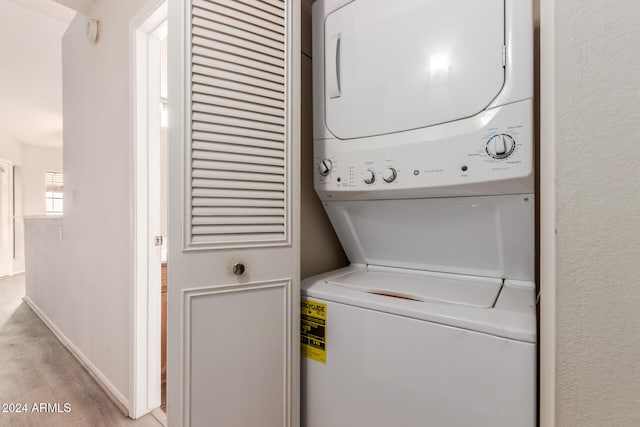 laundry room featuring stacked washer / dryer and light hardwood / wood-style flooring