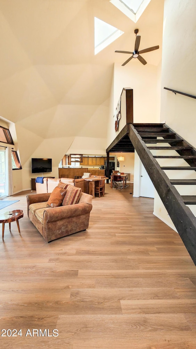 living room with ceiling fan, high vaulted ceiling, a skylight, and light hardwood / wood-style floors