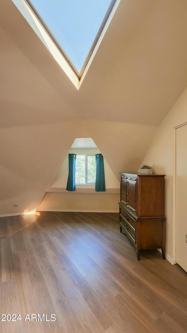 additional living space with vaulted ceiling with skylight and hardwood / wood-style floors