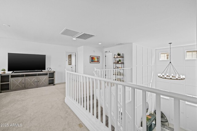 hallway featuring a notable chandelier, visible vents, an upstairs landing, and carpet flooring
