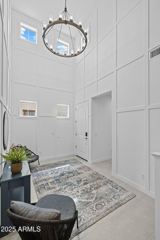 entrance foyer with a notable chandelier, visible vents, a towering ceiling, and a decorative wall