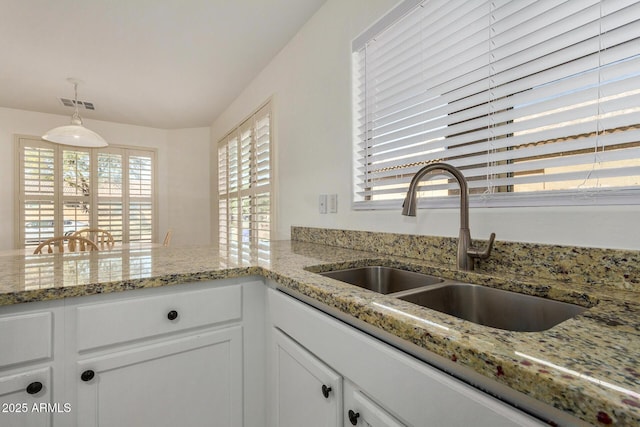 kitchen featuring sink, light stone countertops, white cabinets, and pendant lighting