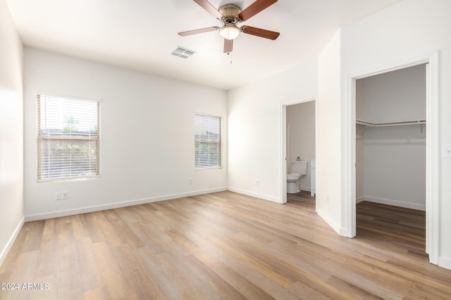 unfurnished bedroom with ensuite bath, light hardwood / wood-style flooring, ceiling fan, a spacious closet, and a closet