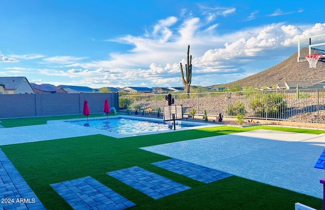 view of swimming pool featuring a patio, a mountain view, a yard, and basketball hoop