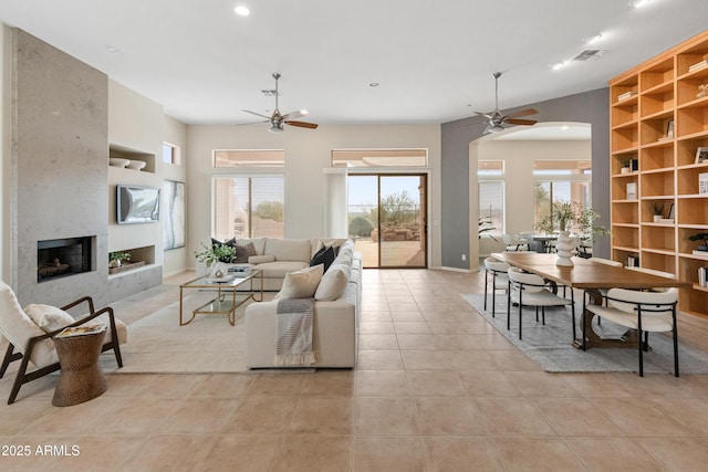 tiled living room with built in features, a large fireplace, and ceiling fan