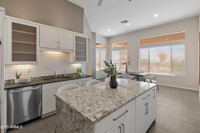 kitchen with sink, dark tile patterned flooring, dishwasher, a kitchen island, and white cabinets