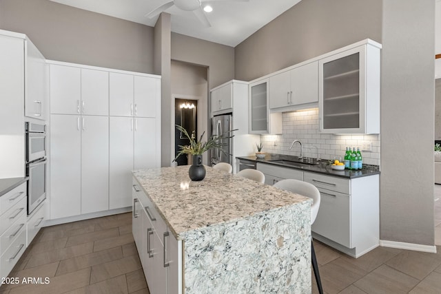 kitchen with sink, appliances with stainless steel finishes, a kitchen island, ceiling fan, and white cabinets