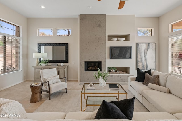 tiled living room with a large fireplace, built in features, and ceiling fan