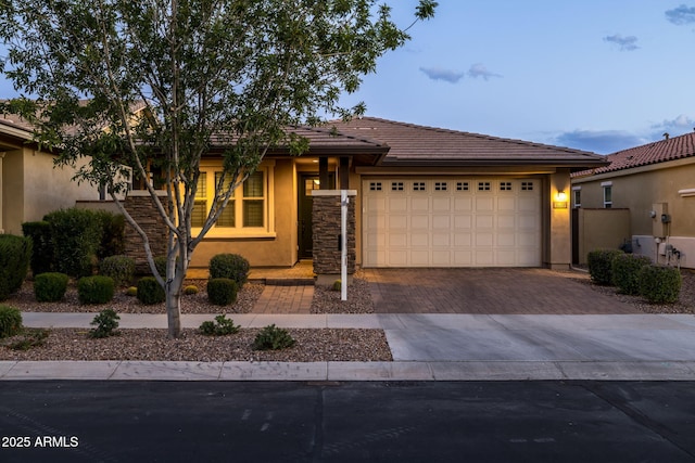 ranch-style home featuring stone siding, a garage, stucco siding, decorative driveway, and a tiled roof