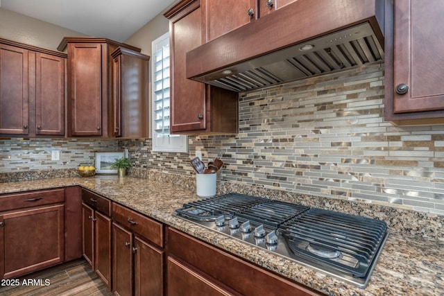 kitchen featuring decorative backsplash, stainless steel gas cooktop, wood finished floors, light stone counters, and wall chimney exhaust hood