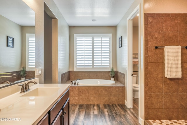 bathroom with toilet, plenty of natural light, wood finished floors, and a garden tub