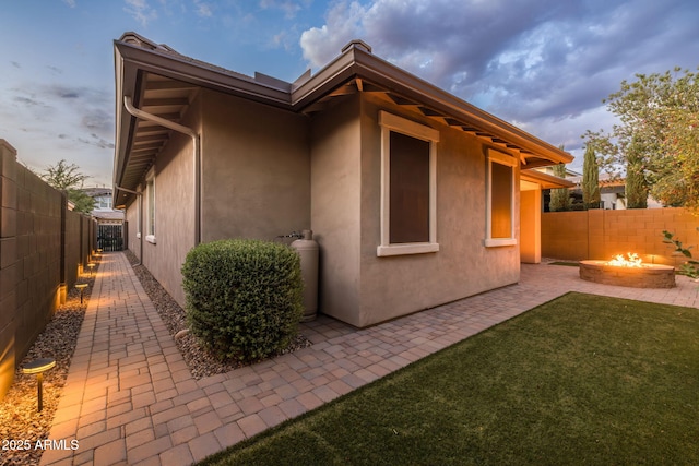 rear view of house featuring a fenced backyard, an outdoor fire pit, a yard, a patio, and stucco siding