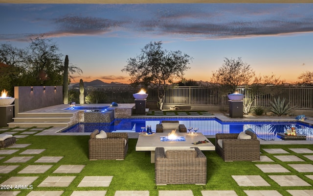 pool at dusk with a patio area, an in ground hot tub, a yard, and an outdoor fire pit