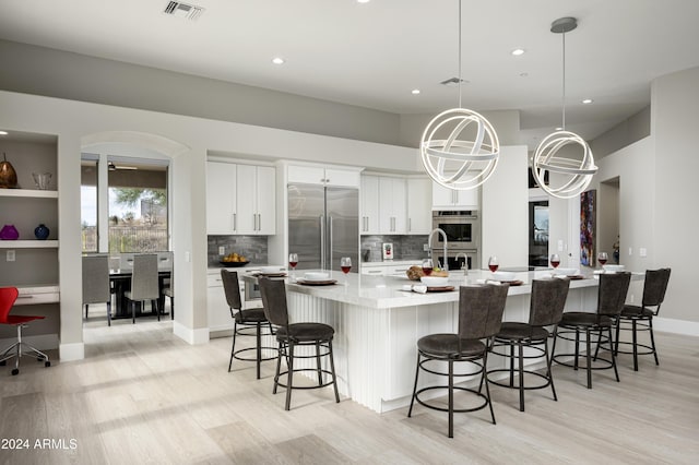 kitchen featuring backsplash, stainless steel appliances, pendant lighting, white cabinets, and an island with sink