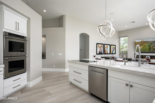 kitchen with white cabinets, sink, appliances with stainless steel finishes, decorative light fixtures, and light stone counters