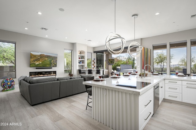 kitchen featuring white cabinets, a kitchen breakfast bar, sink, black electric cooktop, and decorative light fixtures