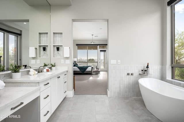 bathroom with vanity, a tub to relax in, plenty of natural light, and tile walls