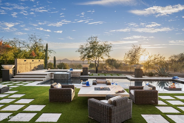 patio terrace at dusk featuring a lawn, a pool with hot tub, and an outdoor fire pit