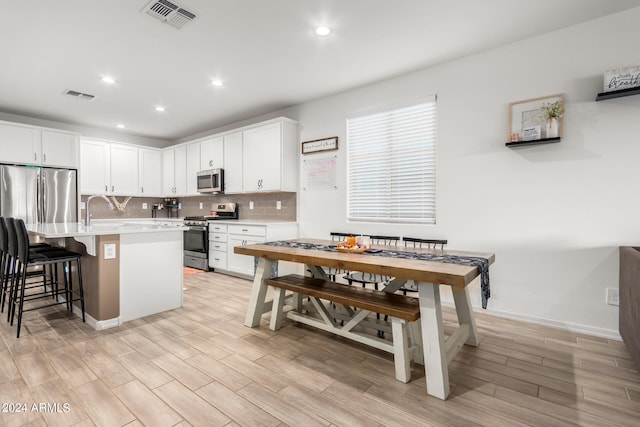 kitchen with appliances with stainless steel finishes, light hardwood / wood-style floors, a kitchen island with sink, and a breakfast bar area