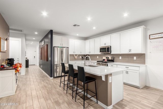 kitchen with appliances with stainless steel finishes, white cabinetry, light wood-type flooring, a kitchen island with sink, and sink