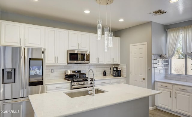 kitchen featuring white cabinetry, light stone counters, decorative light fixtures, a center island with sink, and appliances with stainless steel finishes