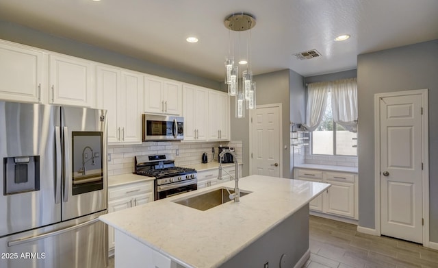 kitchen featuring a kitchen island with sink, sink, appliances with stainless steel finishes, decorative light fixtures, and white cabinetry