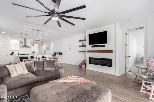 living room featuring light wood-type flooring, ceiling fan, and a large fireplace