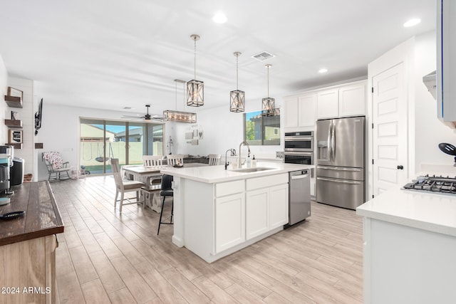 kitchen featuring a center island with sink, stainless steel appliances, white cabinetry, pendant lighting, and sink