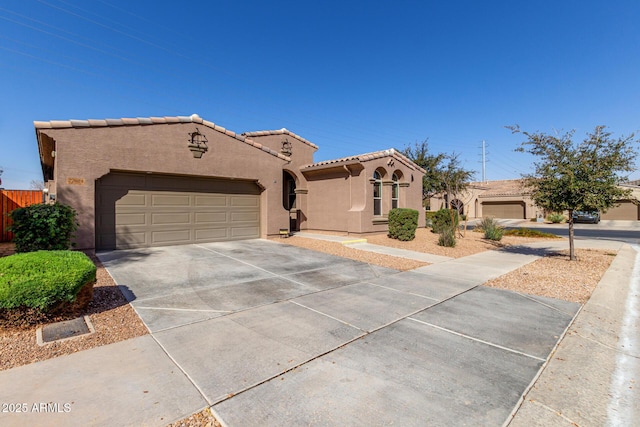 mediterranean / spanish-style house featuring an attached garage, fence, a tiled roof, driveway, and stucco siding