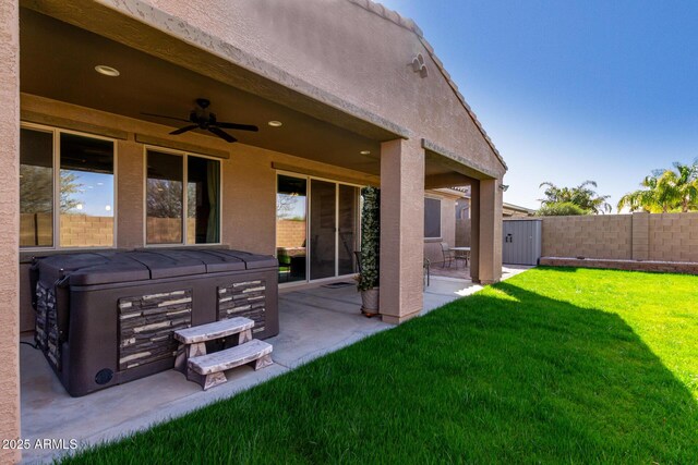 exterior space featuring ceiling fan, a patio, fence, a lawn, and a hot tub