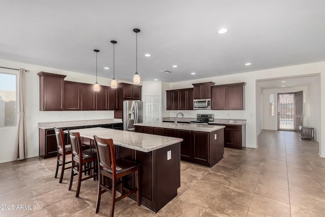 kitchen featuring a kitchen island with sink, recessed lighting, dark brown cabinetry, a sink, and appliances with stainless steel finishes