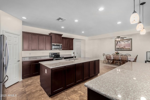 kitchen with decorative light fixtures, stainless steel appliances, visible vents, a sink, and an island with sink