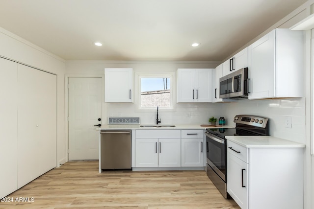 kitchen featuring appliances with stainless steel finishes, sink, white cabinets, decorative backsplash, and light hardwood / wood-style floors