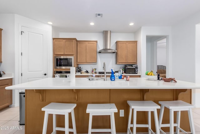 kitchen with a breakfast bar area, a large island with sink, black microwave, and wall chimney range hood