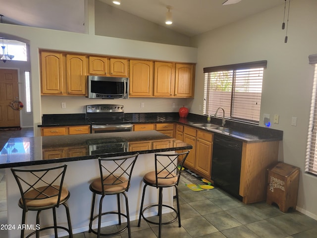 kitchen with dark stone countertops, appliances with stainless steel finishes, sink, a kitchen breakfast bar, and dark tile patterned floors