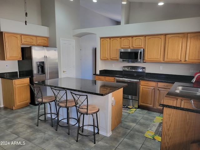 kitchen featuring stainless steel appliances, a breakfast bar, tile patterned floors, a kitchen island, and sink