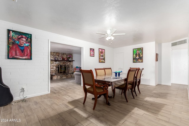 dining room with a fireplace, light wood-type flooring, a textured ceiling, and ceiling fan