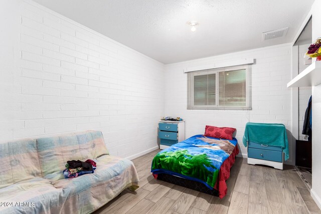 bedroom featuring a textured ceiling, light hardwood / wood-style flooring, and brick wall