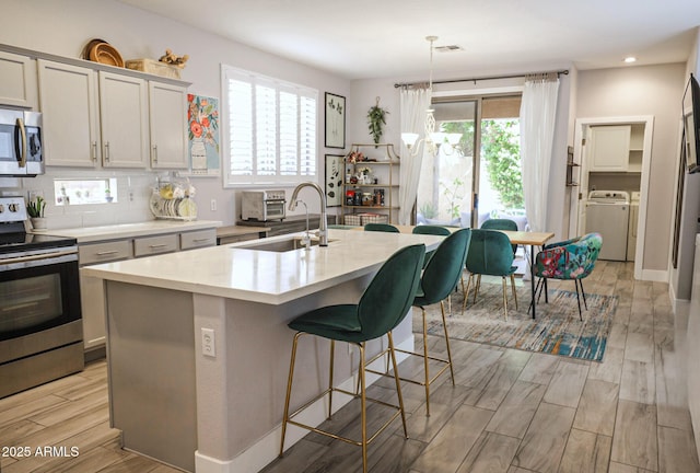 1950 W Park Pl, Chandler, AZ 85224 - kitchen featuring appliances with stainless steel finishes, a sink, a kitchen island with sink, separate washer and dryer, and a breakfast bar area