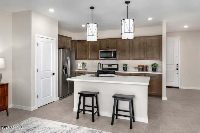 kitchen featuring a kitchen breakfast bar, stainless steel appliances, pendant lighting, decorative backsplash, and a kitchen island with sink