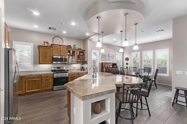 kitchen featuring dark wood-type flooring, a center island with sink, hanging light fixtures, appliances with stainless steel finishes, and a kitchen bar